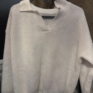 Vit och svart stickad tröja - Säljer en stilren vit och svart stickad tröja med v-ringning och krage. Perfekt för kyliga dagar med sin mjuka och bekväma passform. Tröjan har långa ärmar och en klassisk design som passar till det mesta.