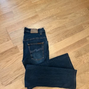 jeans från Nudie Jeans - Snygga mörkblå jeans. En riktigt fet broderad detalj på bakfickan som matcher färgen på jeansen svin snyggt. Perfekta för en stilren look. Knappt använda för dom va för korta för mig. Lätt dom snyggaste jeansen jag ägt.