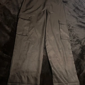 Svarta cargobyxor - Boohoo - Snygga svarta cargobyxor från Boohoo med praktiska fickor på sidorna. Perfekta för en avslappnad stil. Byxorna har en loose passform och är tillverkade i ett bekvämt material.