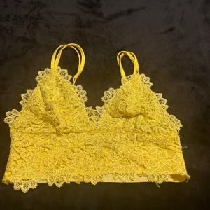 Spetstopp - Bik Bok - Säljer en söt gul spetslinne från Bik Bok med smala axelband. Toppen har ett vackert spetsmönster och är perfekt för varma dagar. Den är i storlek S och ger en feminin touch till din outfit.