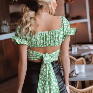 Grön blommig topp med knytband - Säljer en söt grön blommig topp från Shein med puffärmar och knytband i ryggen. Toppen har ett fint blommönster med vita och gula blommor och är perfekt för sommarens varma dagar.