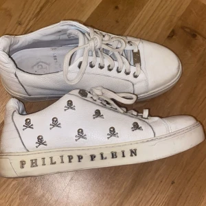 Vita sneakers från Philipp Plein - Stilrena vita sneakers från Philipp Plein med coola dödskalle-detaljer i silver. Skorna har snörning och märkeslogga på sulan. Perfekta för dig som vill ha en edgy look.