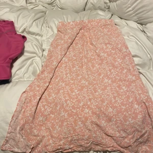 Rosa blommig kjol - Söt rosa långkjol med vitt blommönster. Perfekt för en somrig look. Kjolen har en mjuk och luftig design som ger en romantisk känsla.