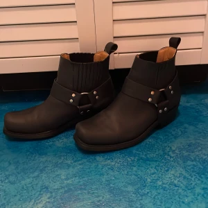 Svarta boots med spänne - Snygga svarta boots från Durango med dekorativa spännen och nitar. De har en robust sula och är perfekta för en cool look. Passar bra till både jeans och läderjacka. Pris går att förhandla 🥰