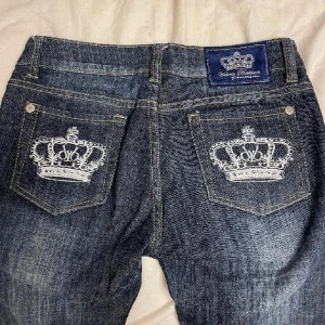 Lågmidjade victoria beckham jeans - Snygga mörkblå jeans från Victoria beckham, storlek 27. Unika broderade kronmotiv på bakfickorna. Enda defekt är att några kristaller där back saknas. Jeansen har en straight 00’s passform. Pris kan diskuteras!