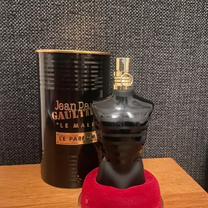 Jpg Le Male Le Parfum parfym  - Säljer en elegant parfymflaska formad som en manlig torso i svart med gulddetaljer. Flaskan rymmer 75 ml av doften Le Male Le Parfum, känd för sin intensiva och förföriska doft. Kommer i en stilren svart metallförpackning.