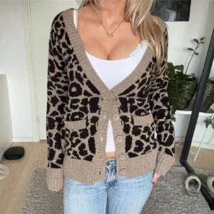 leopardmönstrad kofta - Snygg beige kofta med leopardmönster och knappar framtill. Den har långa ärmar och ribbade kanter. Perfekt för att ge din outfit en trendig touch.