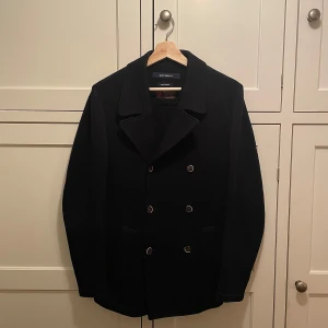 Suitsupply Peacoat, Navy Blue, Storlek 48 –  - suto Italiano • Tillverkad i Italien • Skick: Utmärkt, aldrig använd  En tidlös och elegant peacoat tillverkad av högkvalitativt italienskt tyg. Perfekt för både formella och avslappnade tillfällen, och erbjuder både stil och komfort. Perfekt för en stilren look. Fraktar samma dag köpet genomförs. 