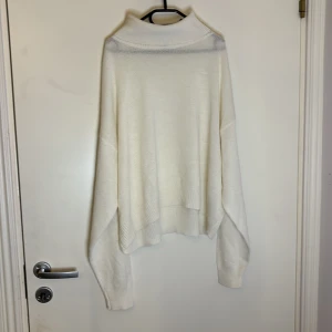Vit tun stickad tröja - Säljer en stilren vit tun stickad med långa ärmar. Tröjan har en ribbad polokrage och är perfekt för kyligare dagar. Den är mjuk och bekväm, vilket gör den till ett utmärkt val för både vardag och mysiga stunder hemma. Smink fläk på kragen sista bilden.
