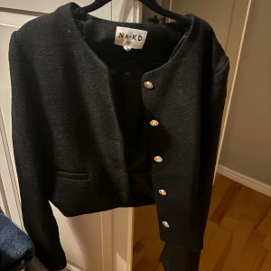 Svart kofte från NA-KD - Snygg svart kofta från NA-KD med guldknappar. Perfekt för en stilren look. Kavajen har en klassisk design med långa ärmar och en elegant passform.