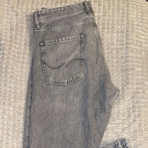 Grå jeans från Jack & Jones - Snygga grå jeans från Jack & Jones med klassisk femficksdesign. De har en normal passform och är perfekta för en dagens stil. Jeansen har en knappgylf och bälteshällor.