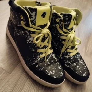 Svarta och gröna sneakers med mönster - Coola sneakers med svart och vit mönsterdesign och gröna detaljer. Skorna har snörning och en högre modell som ger extra stöd. Perfekta för en unik och trendig stil.