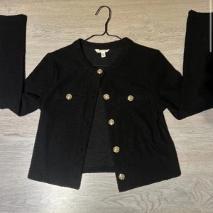 Svart kavaj med guldknappar - Elegant svart kavaj med dekorativa guldknappar. Perfekt för en stilren look. Kavajen har en klassisk design med långärmade ärmar och en bekväm passform. Priset går att diskutera