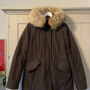 Brun dunjacka från Woolrich XL - En varm vinterjacka/dunjacka med huva och pälskant. Jackan har två fickor på framsidan och en innerficka. Den är i bra skick.  Woolrich Vail Parka i mörkbrun färg - storlek XL men tycker Woolrich är lite mindre i storleken och skulle säga att denna sitter som en normal L.  Vatten och vindtät samt i fint skick.  Finns att hämta på Lilla Essingen eller kan skickas spårbart.