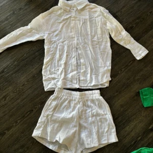 Vit skjorta med matchande shorts - Säljer en vit skjorta med långärmad design och knappar framtill. Skjortan har en avslappnad passform och är tillverkad i ett lätt material. Perfekt för varma dagar.
