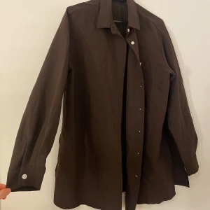 Brun skjorta med knappar -  Brun skjorta med långa ärmar och knappar. Är ett set. Använd endast en gång. Passar 36-40