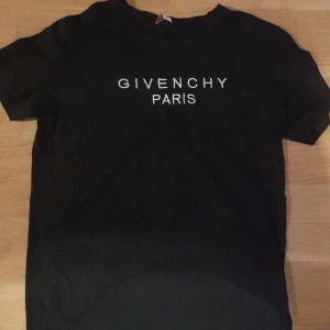 Svart t-shirt från Givenchy - Snygg svart t-shirt från Givenchy med vit text 'GIVENCHY PARIS' på framsidan. T-shirten har korta ärmar och Givenchy-logga längs axlarna. Perfekt för en stilren look. OPS! Se defekt på bild 3. Passar dig mellan 155-165cm