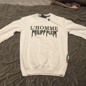 Vit tröja från Philipp Plein - Säljer en stilren vit tröja från Philipp Plein med texten 'L'HOMME PHILIPP PLEIN' tryckt på framsidan. Tröjan är i nyskick och väldigt fin.