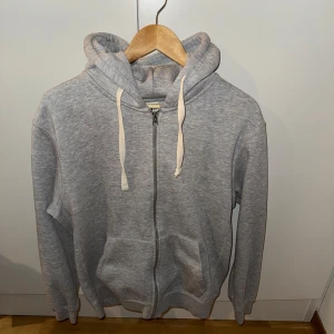 Grå zip-hoodie från Zara - Säljer en stilren grå hoodie från Zara med dragkedja och huva. Perfekt för en avslappnad look. Den har långa ärmar och en mjuk insida för extra komfort. Tröjan är i bra skick och köpt på man avdelningen men sett samma tröja användas av tjejer också därav unisex.