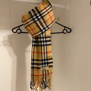 Burberry - Säljer nu denna Snygga och klassiska halsduk från Burberry i beige. Tillverkad i mjukt lammull med fransar i ändarna. Perfekt för att hålla dig varm och stilren under kyliga dagar. Hör av er vid funderingar☺️
