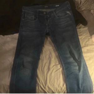 Blå jeans från Replay - Säljer ett par snygga blå jeans från Replay, modell Anbass. De har en klassisk femficksdesign med knappgylf och subtila slitningar för en trendig look. Perfekta för en avslappnad stil. De är storlek W34 men skulle säga att de passar W32 eftersom de är slimfit.
