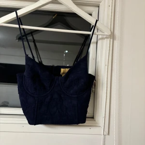 Mörkblå korsettopp från Zara - Snygg mörkblå korsettopp från Zara med smala axelband och hakknäppning bak. Toppen har ett elegant mönster och är perfekt för en stilren look. Tillverkad i polyester med en liten del elastan för stretch.