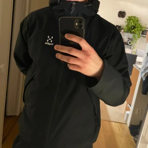 Svart vindjacka från Haglöfs - Säljer en stilren svart vindjacka från Haglöfs. Jackan har en praktisk huva och dragkedja framtill. Perfekt för Sverige väder storlek L inte använt så mycket därmed säljer jag den