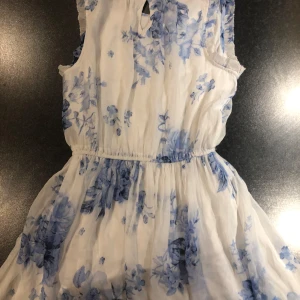 Vit och blå blommig klänning från Hampton Republic - Charmig vit klänning med blått blommönster från Hampton Republic. Klänningen är ärmlös och har en luftig design med elastisk midja för en bekväm passform. Perfekt för somriga dagar.