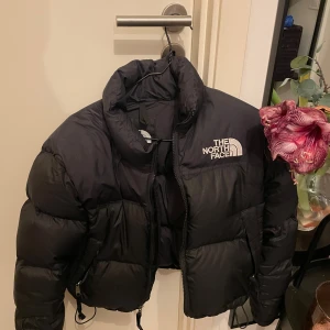 Svart pufferjacka från The North Face - Säljer en svart pufferjacka från The North Face. Jackan har en hög krage och dragkedja framtill. Köptes här på Plick men missade att modellen är short nuptse. Helt utan defekter. Använd en vinter av förra ägaren. 