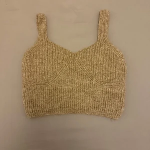 Beige topp från NA-KD - Säljer en snygg beige topp från NA-KD. Toppen har breda axelband och en croppad passform, perfekt för lager-på-lager eller som den är. Ett stilrent plagg som passar till många olika outfits.