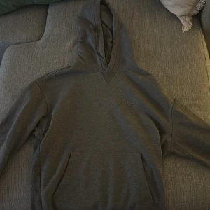 Grå hoodie från BOSS - Säljer en stilren grå hoodie från BOSS med en diskret logga på bröstet. Tröjan har en klassisk känguruficka och en bekväm huva. Perfekt för en avslappnad look.