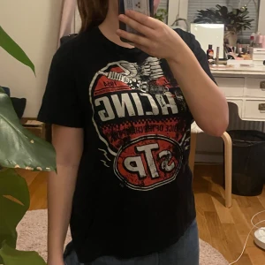 Svart t-shirt med STP Racing-tryck från Gildan - Cool svart t-shirt från Gildan med ett stort STP Racing-tryck i rött och vitt. Perfekt för racingfans som vill ha en avslappnad stil. T-shirten är kortärmad och gjord i mjuk bomull. Har dock en fläck så priset kan diskuteras💕