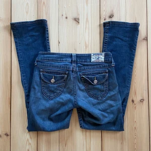 Jeans bootcut True Religion - Säljer ett par supersnygga och bekväma bootcut-jeans från True Religion då de är lite för stora för mig. Modellen heter ’Hi-rise boot’ men jag skulle snarare säga att de är midrise. Fickorna är av äldre modell - gissar att jeansen är från tidigt 2000-tal. Innerbenslängden är 75cm, de är några cm för långa på mig som är 160cm. W27/S. Inga märkbara skavanker vad jag kan se. Skicka gärna meddelande om du vill ha fler bilder eller har frågor :)