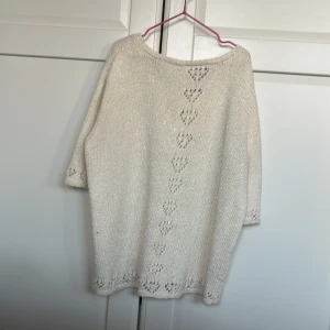 Vit stickad tröja med hjärtmönster - Säljer en söt vit stickad tröja med hjärtmönster längs framsidan. Tröjan har trekvartsärmar och en rund halsringning. Perfekt för en mysig dag.