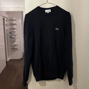 Marinblå tröja från Lacoste - Säljer en stilren marinblå tröja från Lacoste i S. Tröjan har en klassisk design med det ikoniska krokodilmärket på bröstet. Perfekt för en avslappnad och snygg look. Köptes för runt 1000kr på åhlens. 