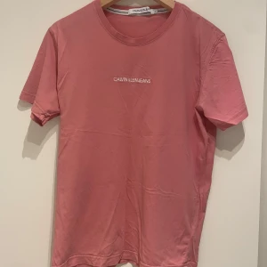 Rosa t-shirt från Calvin Klein - Snygg rosa t-shirt från Calvin Klein med korta ärmar och rund halsringning. Perfekt för en avslappnad stil. Calvin Klein Jeans-loggan är tryckt på bröstet.