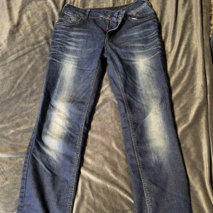 Blå jeans från ONLY - Säljer ett par blå jeans från ONLY i modellen Aisha Low Slim. De har en snygg tvätt med ljusare partier och en klassisk femficksdesign. Perfekta för en avslappnad stil.