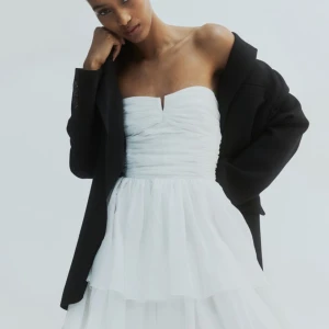 Vit axelbandslös klänning - Elegant vit axelbandslös klänning med volangdetaljer och en kort längd. Perfekt för sommaren och som studentklänning!! Klänningen är aldrig använd✨ Köptes för 700kr men säljer den för 299 så det blir en riktigt bra deal👌🏼 skriv gärna om du är intresserad eller har frågor🫶🏼💕