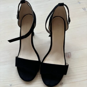 Svarta klackskor från Bianco - Snygga svarta klackskor från Bianco med öppen tå och justerbart spänne runt ankeln. Perfekta för en elegant look.