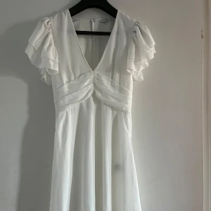 Vit klänning/ studentklänning från Bubbleroom - Elegant vit klänning från Bubbleroom med v-ringning och volangdetaljer på ärmarna. Perfekt för speciella tillfällen.
