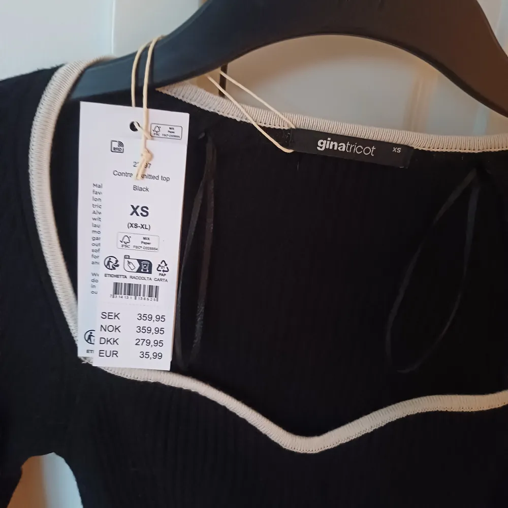 Snygg svart ribbad topp från Gina Tricot med kontrasterande vit kant vid halsringningen. Toppen har långa utsvängda ärmar och en tight passform, perfekt för en stilren look. Aldrig använd. Yläosat.