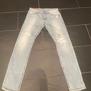 Ljusblå dundup jeans med slitningar - Säljer ett par ljusblå jeans med coola slitningar och en klassisk femficksdesign. De har en knappgylf och är perfekta för en avslappnad stil. Passar bra utmärkt med ett par feta skor. Storleken är 33 och märket är dundup. Ett stilrent märke. Byxorna passar till allt. Hör av er om några fler funderingar🙏.                                         Nypriss: 2700kr                                                     Mitt pris: 1035kr