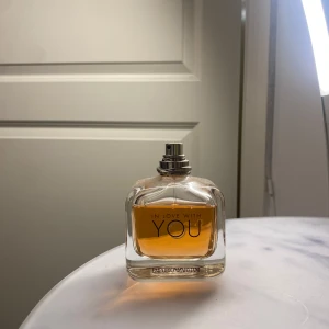 In Love With You parfym - Elegant parfymflaska från Emporio Armani med namnet 'In Love With You'. Flaskan är genomskinlig med en stilren design och innehåller en gyllene doftvätska. Perfekt för den som söker en sofistikerad och romantisk doft. Locket saknas.
