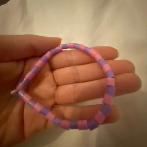 Färgglada armband och hårband - Säljer ett set med färgglada armband och hårband. Armbandet är gjort av rosa och lila pärlor. Hårbanden kommer i olika färger som lila, röd och beige, och ett av dem har en dekorativ rosett med pärlor.