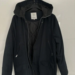 Mörkblå vinterjacka från Elvine - Mörkblå svart vinterjacka från Elvine med huva och dragkedja. Jackan har långa ärmar och praktiska fickor med dragkedjor. Perfekt för kyligare dagar.