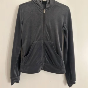 Grå hoodie från Gina Tricot - Mysig grå hoodie från Gina Tricot med dragkedja och huva. Perfekt för en avslappnad stil. Tillverkad i mjukt material med långa ärmar och praktiska fickor framtill.