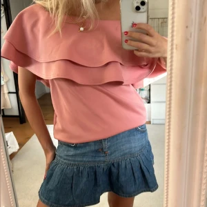 korall-färgad offshoulder topp med volang - Säljer en söt korall färgad offshoulder topp med volangdetaljer. Perfekt för en somrig look. Toppen har en lös passform och är tillverkad i ett mjukt material.