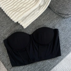 Svart korsett-topp - Snygg svart korsett-topp med strukturerade kupor och en tight passform. Perfekt för en stilren look.