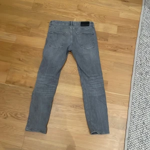 Grå jeans från Jack & Jones - Säljer ett par grå jeans från Jack & Jones i modellen Regular Clark. De har en klassisk femficksdesign med knapp och dragkedja framtill. Perfekta för en avslappnad stil.