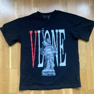 Svart t-shirt Large Frihetsgudinnan Vlone - Cool svart t-shirt från Vlone med ett stort tryck av Frihetsgudinnan och texten 'VLONE' i rött och vitt. Perfekt för streetwear-stilen.  Oversized fit. Det står medium men den sitter som en Large. Bara testad en gång